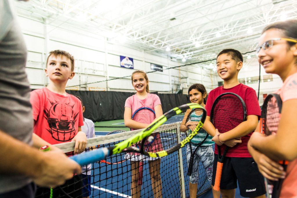 Groupe d'enfants tenant des raquettes de tennis regardant un entraîneur et souriant
